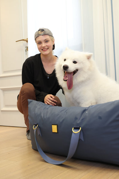 Samoyed and owner at home beside the navy dog car seat bed used as an everyday dog bed on the floor